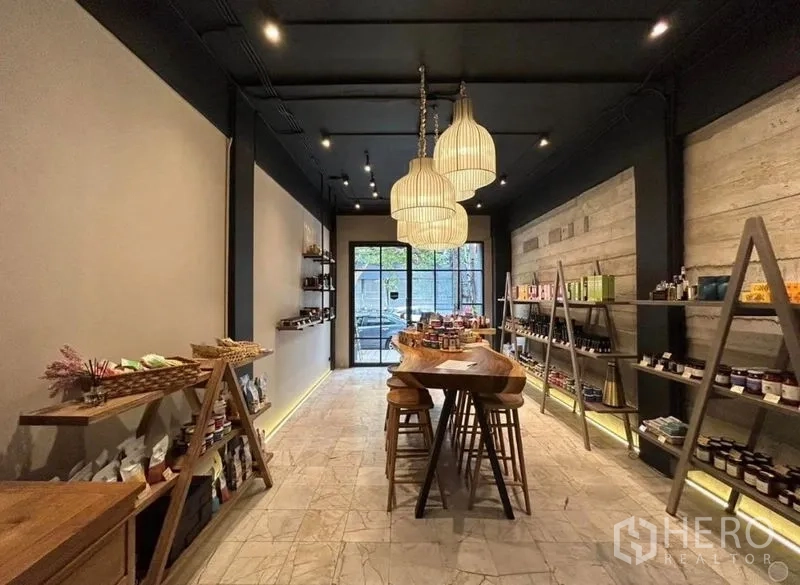 Retail Space for rent in Bang Rak, Bangkok - Warm-lit retail shop interior with wood display table, pendant lights, open shelving and a glass front door.