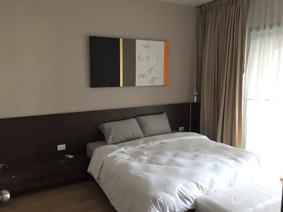 Condominium for rent in Watthana, Bangkok - Master bedroom with dark wood headboard, modern wall art, floor‑to‑ceiling curtains and soft natural light in a Watthana Bangkok condo.
