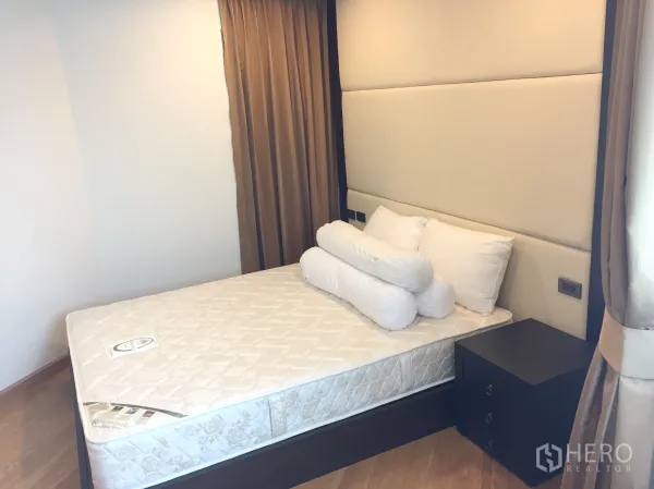 Condominium for rent in Sathon, Bangkok - Cozy bedroom with padded headboard, bedside table and thick blackout curtains.