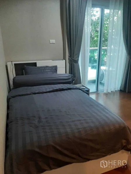 Condominium for rent or sale in Huai Khwang, Bangkok - Bedroom with a single bed and sliding glass doors to a balcony facing greenery.