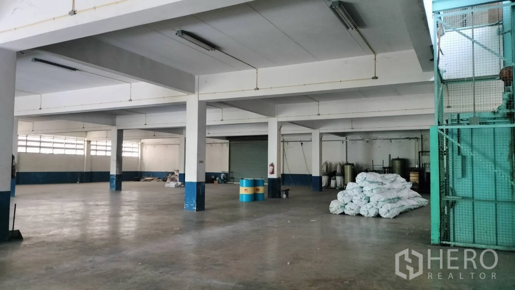 Factory for rent in Lat Krabang, Bangkok - Open warehouse area with support columns, high windows, and stacked bags on the concrete floor.