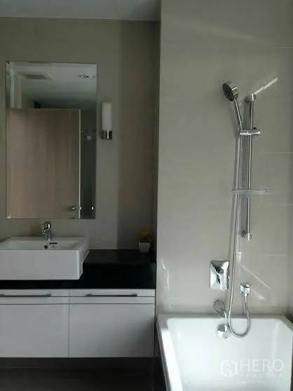 Condominium for rent or sale in Huai Khwang, Bangkok - Modern bathroom with vanity and mirror alongside a bathtub with handheld shower.