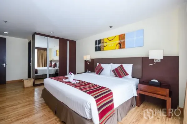 Condominium for rent in Khlong Toei, Bangkok - Spacious bedroom with king bed, bedside tables, colorful artwork and mirrored wardrobe.