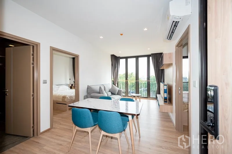 คอนโด ให้เช่าในWatthana, Bangkok - พื้นที่นั่งเล่นและรับประทานอาหารสว่างโปร่ง โต๊ะหินอ่อน เก้าอี้สีน้ำเงิน โซฟา และหน้าต่างเต็มบานเปิดสู่ระเบียง
