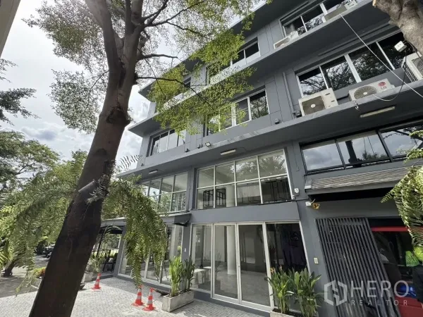 店屋 出租在Wang Thonglang, Bangkok - 建筑正面近景，大片窗户与推拉玻璃门，入口绿植点缀。