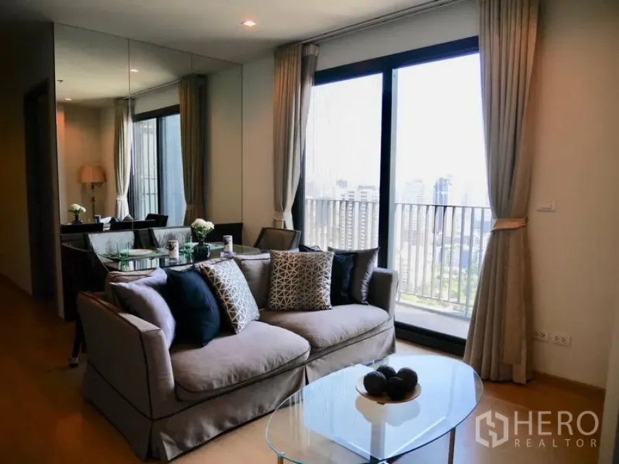 公寓 出租在Watthana, Bangkok - 明亮客厅，沙发与玻璃茶几，落地推门连阳台，俯瞰曼谷天际线。