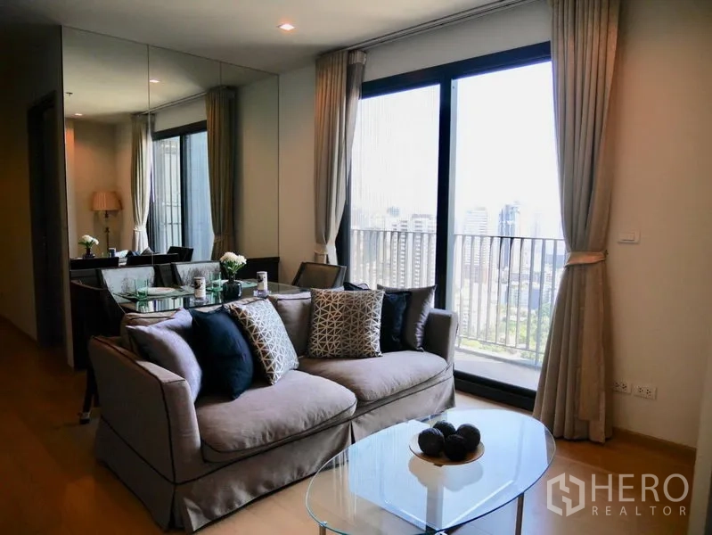 公寓 出租在Watthana, Bangkok - 明亮客厅，沙发与玻璃茶几，落地推门连阳台，俯瞰曼谷天际线。