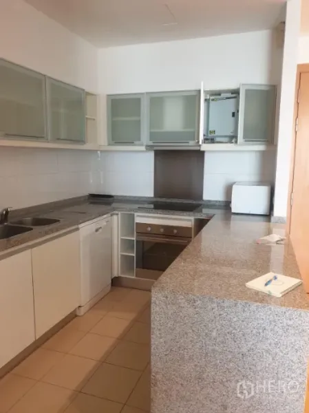Condominium for rent or sale in Khlong Toei, Bangkok - U-shaped kitchen with granite countertops, built-in oven, dishwasher, and glass-front cabinets.
