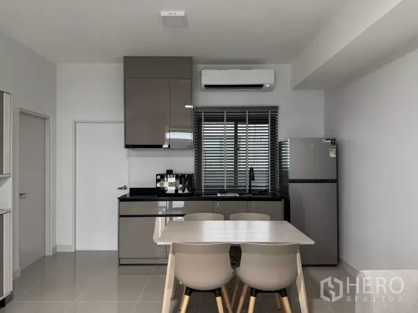 Townhouse for rent in Bang Phli, Samut Prakan - Compact kitchen with upper cabinets, sink, refrigerator and a four-seat dining table.