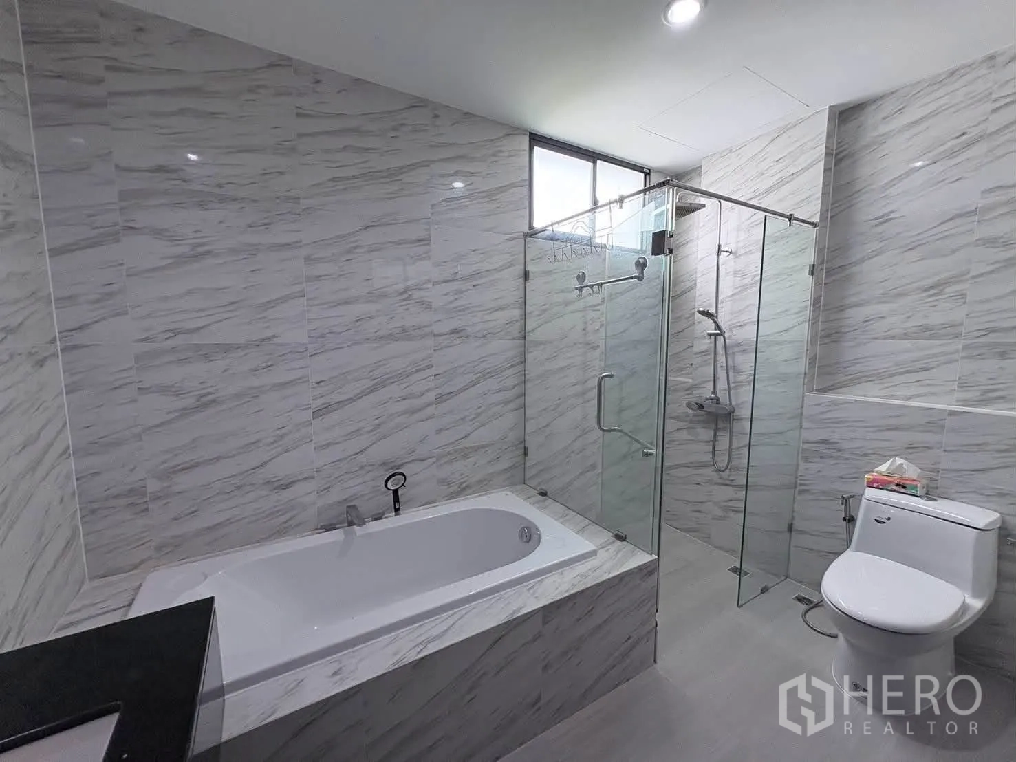 Detached House for rent in Saphan Sung, Bangkok - Modern bathroom with marble-look tiles, bathtub, glass shower enclosure, and toilet.