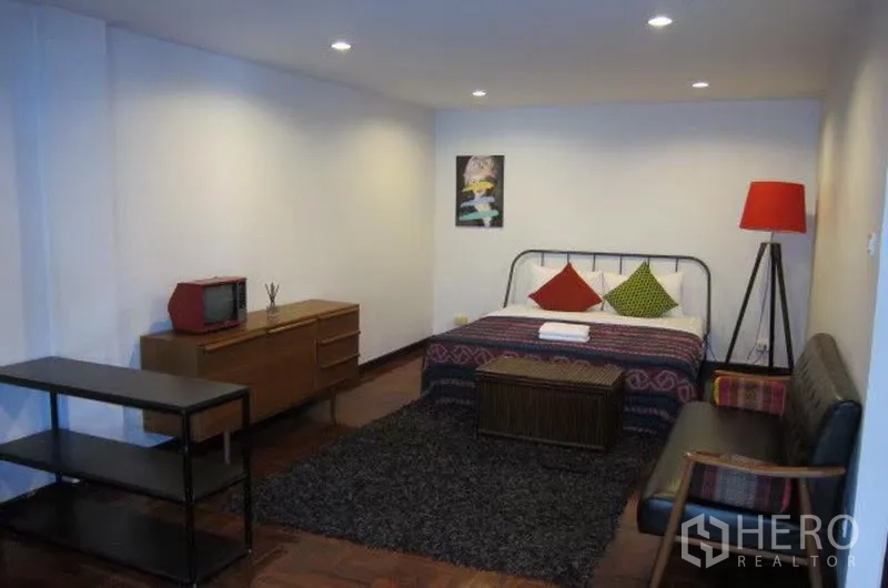 Townhouse for rent in Khlong Toei, Bangkok - Large bedroom with bed, rug, sideboard, recessed lighting and red floor lamp.