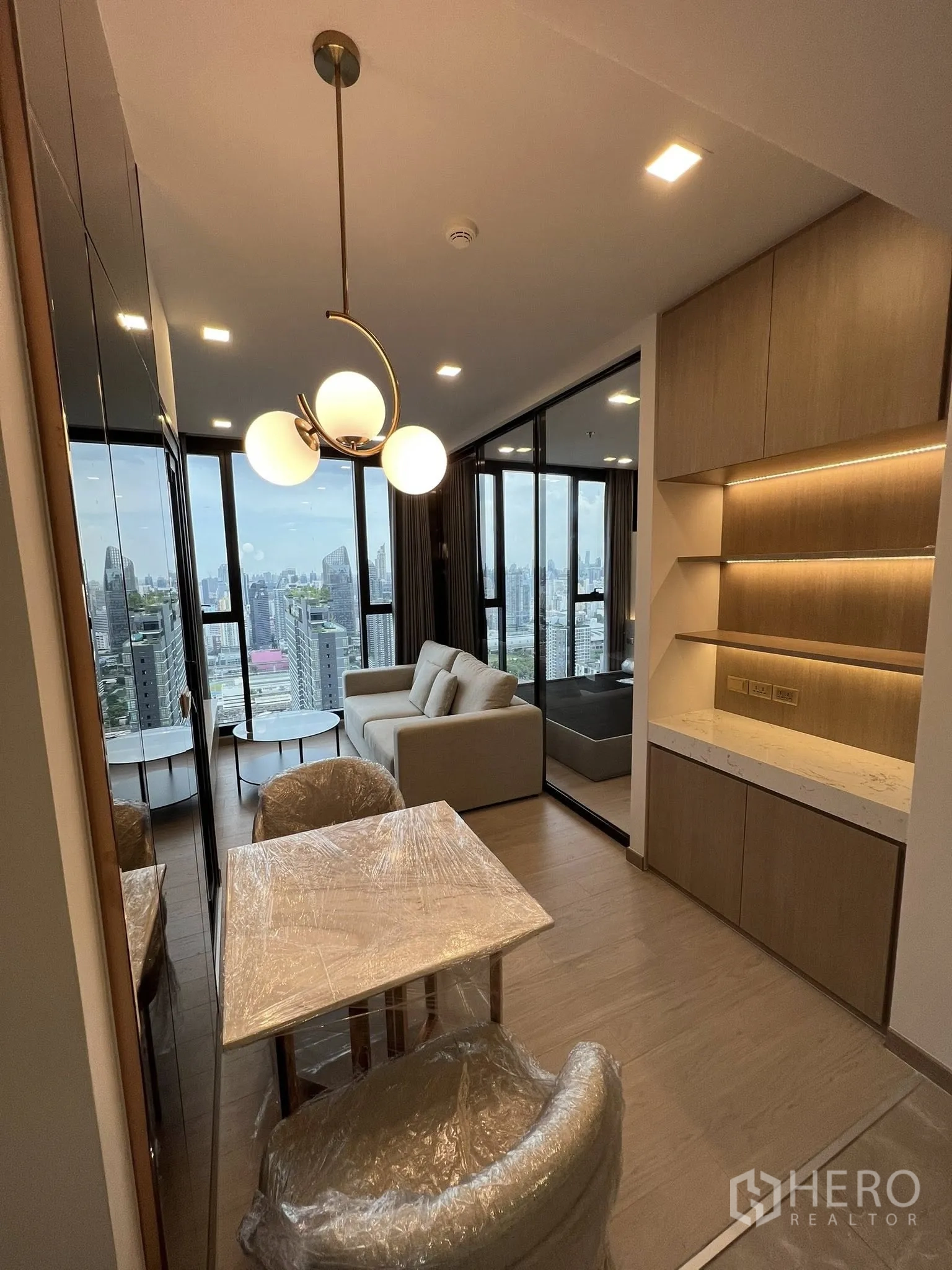 公寓 for rent in Huai Khwang, Bangkok - 开放式客餐厅，吊灯点缀，小餐桌与玻璃隔断卧室，眺望城市天际线。