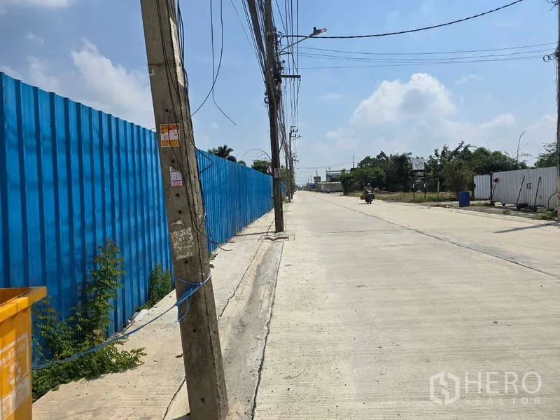 Warehouse for rent in Khlong Sam Wa, Bangkok - Wide access road with power lines and a blue fence near the industrial property.