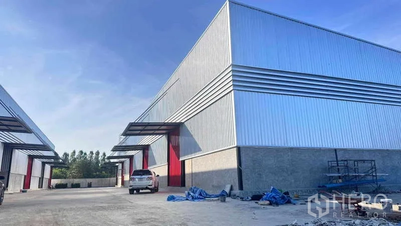 货栈 出租在Khlong Sam Wa, Bangkok - 金属板外墙仓库外观，红色大门，车道与停车区域。