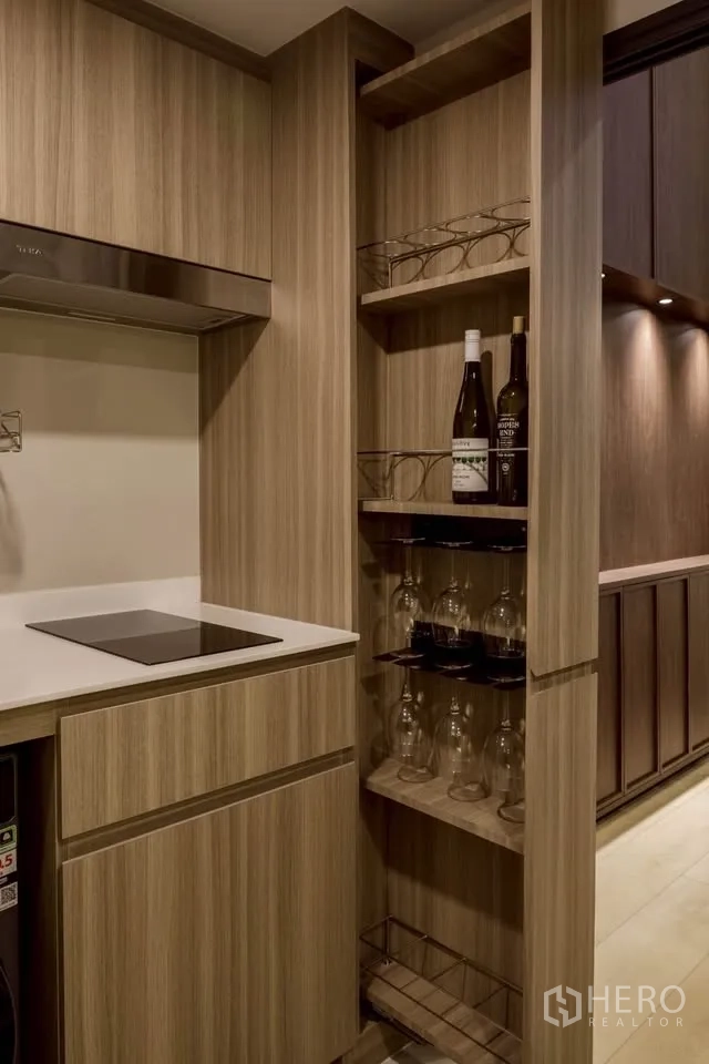 Condominium for rent in Khlong Toei, Bangkok - Compact kitchen with wood cabinetry, induction cooktop, and pull-out pantry wine rack.