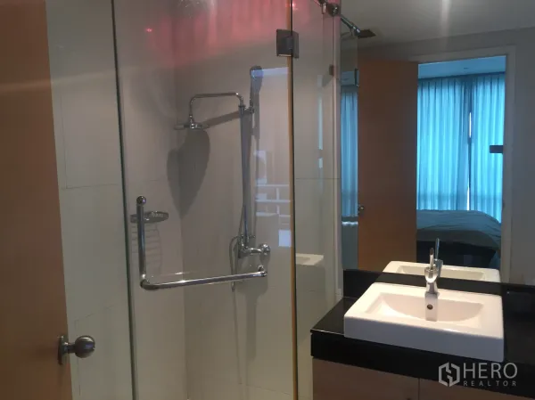 Condominium for rent or sale in Watthana, Bangkok - Modern bathroom with a glass-enclosed shower and white basin on a black countertop.