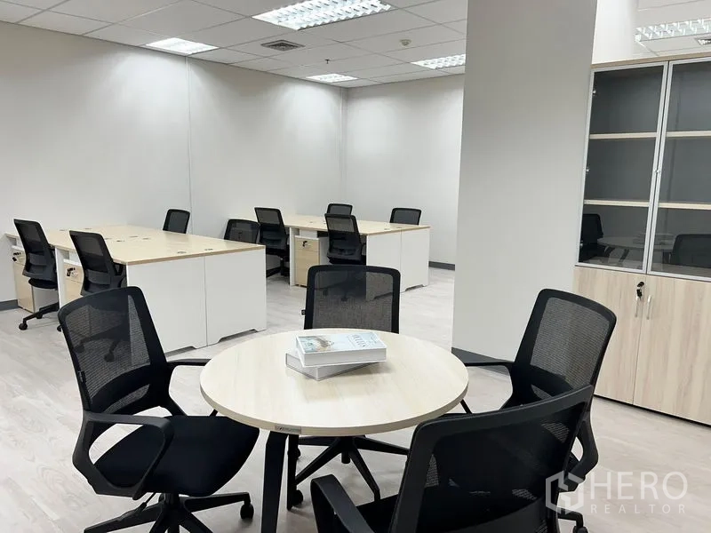 Office Space for rent in Sathon, Bangkok - Round meeting table beside rows of work desks and a storage cabinet in a modern office.