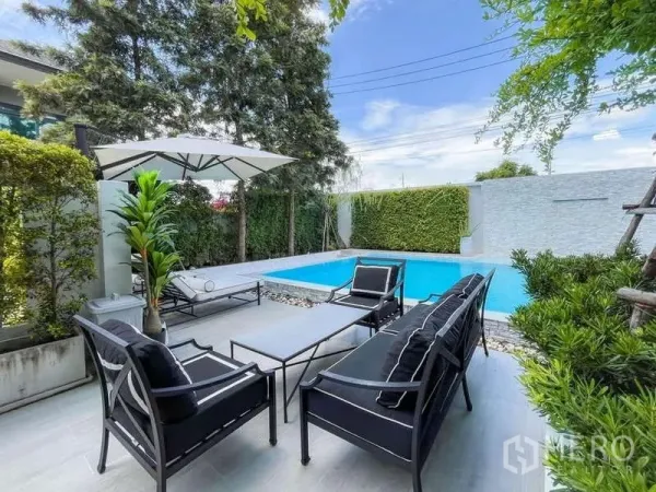 Detached House for sale in Bang Lamung, Chon Buri - Sunny patio with black outdoor lounge furniture, umbrella and hedge‑lined private pool.
