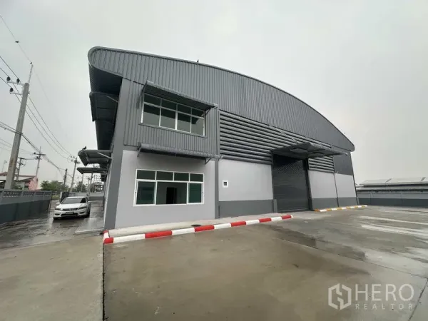 Factory for rent in Pathum Thani - Front facade of steel-clad factory showing roller shutter loading bay and parking apron.