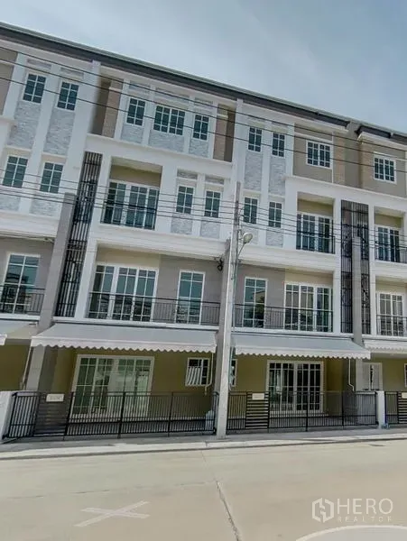 联排别墅 出售在Bang Na, Bangkok - 曼谷邦那区现代多层联排别墅外观，带阳台、大窗、雨篷与带门车位，临街安静。