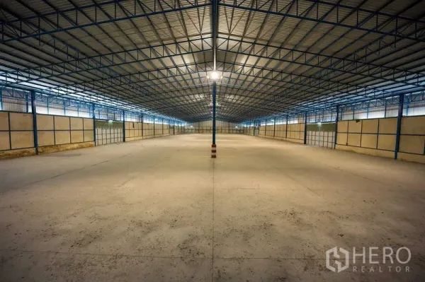 Warehouse for rent in Phra Phutthabat, Saraburi - Expansive open-plan storage hall with blue steel beams, central lighting column, and gated bays.