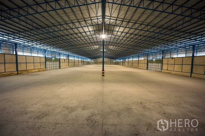 Warehouse for rent in Phra Phutthabat, Saraburi - Expansive open-plan storage hall with blue steel beams, central lighting column, and gated bays.