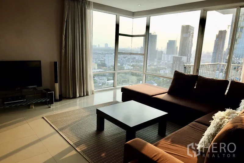 Condominium for rent in Watthana, Bangkok - Corner living area with wraparound windows showcasing the Bangkok skyline at sunset.