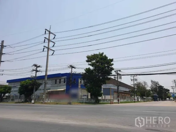 工厂 出租在Bang Pakong, Chachoengsao - 临主干道的工业园街景，可见电线、树木与周边围栏。