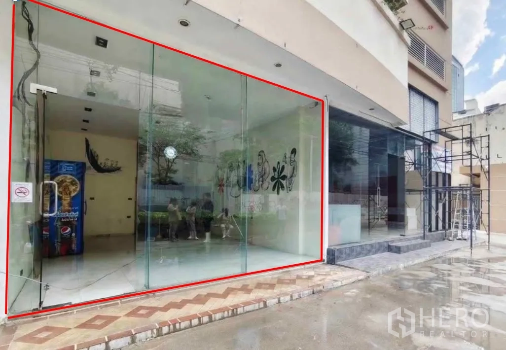 Retail Space for rent in Khlong Toei, Bangkok - Full-height glass storefront of the retail space highlighted beside a neighboring building and paved forecourt.