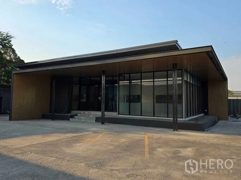 带办公室的家 出租在Prawet, Bangkok - 现代单层玻璃立面办公楼，前方宽阔停车区。