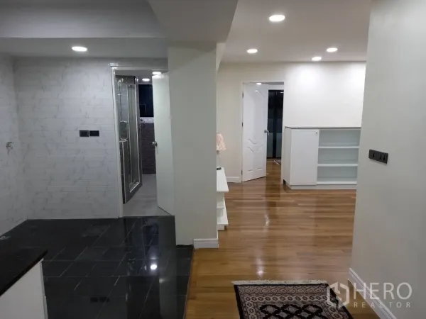 公寓 出租在Khlong Toei, Bangkok - 走廊连通黑色地砖的厨房与木地板起居区，白墙与筒灯明亮。