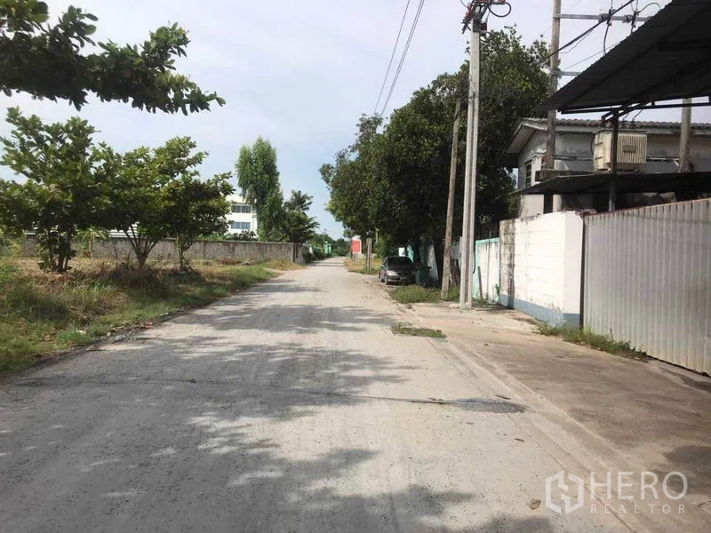 Factory for rent in Bang Phli, Samut Prakan - Quiet access road to the industrial property lined with trees and utility poles.