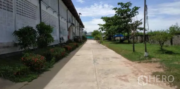 Factory for rent in Bang Pakong, Chachoengsao - Side walkway along a factory wall with garden beds and open green space for easy truck access.