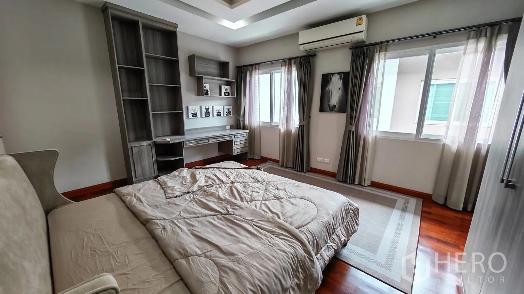 Detached House for rent or sale in Bang Phli, Samut Prakan - Bedroom showing multiple windows, air conditioner, and an area rug on polished wooden flooring.