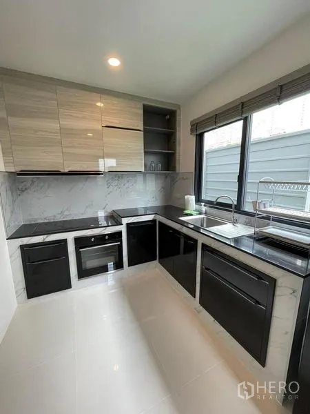 Detached House for rent in Don Mueang, Bangkok - Built-in kitchen with black countertops, cooktop, oven and marble-style backsplash.