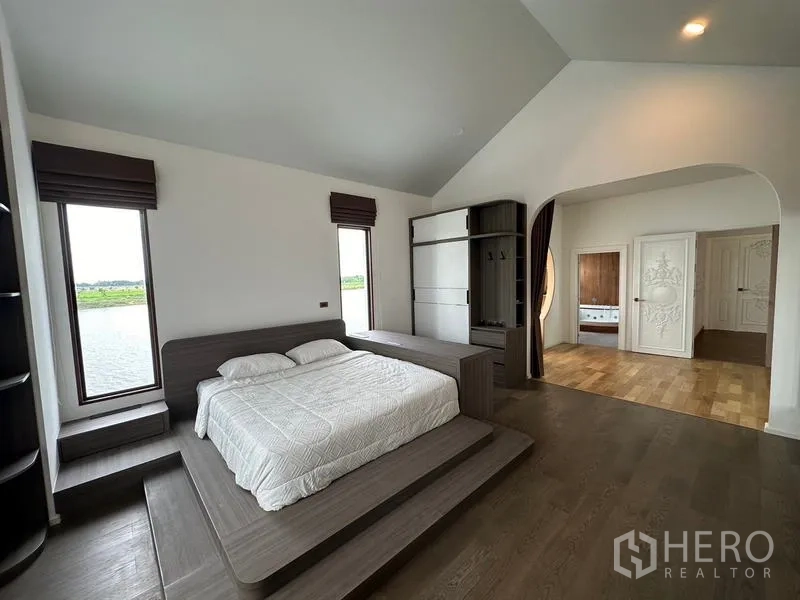 Detached House for sale in Sai Noi, Nonthaburi - Spacious master bedroom with platform bed, arched entry and built‑in wardrobe facing the lake.