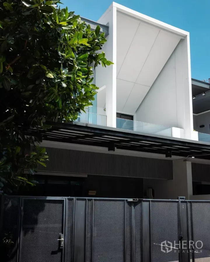 独立式住宅 出租或出售在Bang Phli, Samut Prakan - VIVE Bangna 现代独栋别墅外立面，白色几何阳台与黑色前门围栏，旁有绿树。