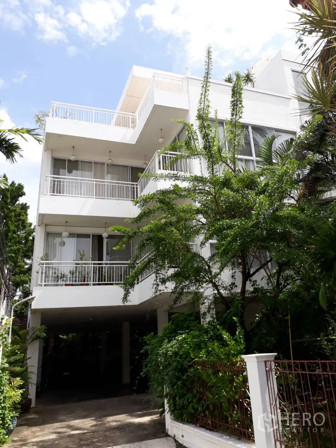 Condominium for rent in Watthana, Bangkok - Exterior of a low-rise white condominium with wide balconies, large windows, greenery and covered parking.