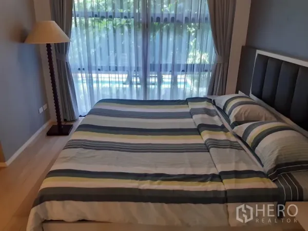 คอนโด ให้เช่าในWatthana, Bangkok - ห้องนอนสว่างโปร่ง เตียงคิงไซส์ ผ้าปูที่นอนลายทาง และหน้าต่างสูงจรดเพดานพร้อมผ้าม่านมองเห็นวิวสีเขียว