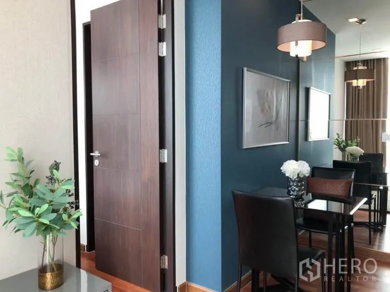 Condominium for rent or sale in Ratchathewi, Bangkok - Hallway with open wooden door, blue feature wall, mirrored panels, and a two-seat dining set.