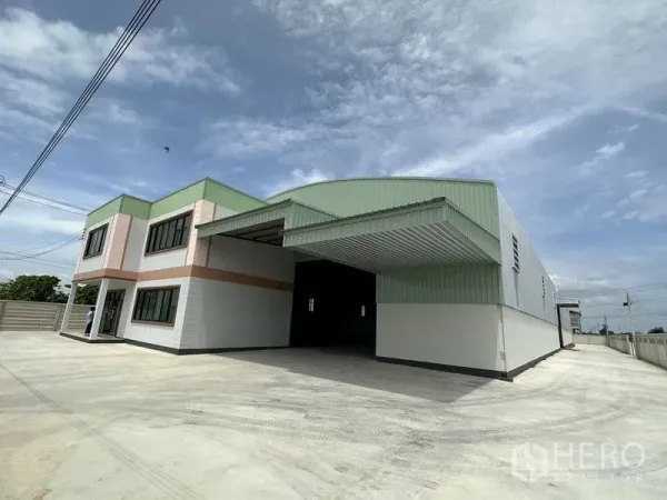 工厂 出租或出售在Sai Noi, Nonthaburi - 外观斜拍，展示有顶装卸区与大型混凝土院场及钢结构外立面。