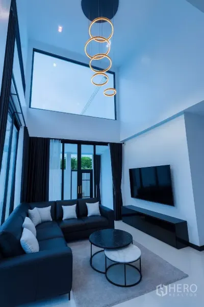 บ้าน ให้เช่าในWang Thonglang, Bangkok - ห้องนั่งเล่นเพดานสูงพร้อมโคมไฟวงแหวน โซฟาเข้ามุม และหน้าต่างเต็มผนัง