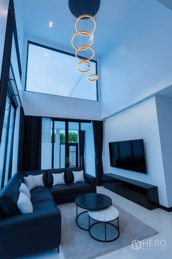 บ้าน ให้เช่าในWang Thonglang, Bangkok - ห้องนั่งเล่นเพดานสูงพร้อมโคมไฟวงแหวน โซฟาเข้ามุม และหน้าต่างเต็มผนัง