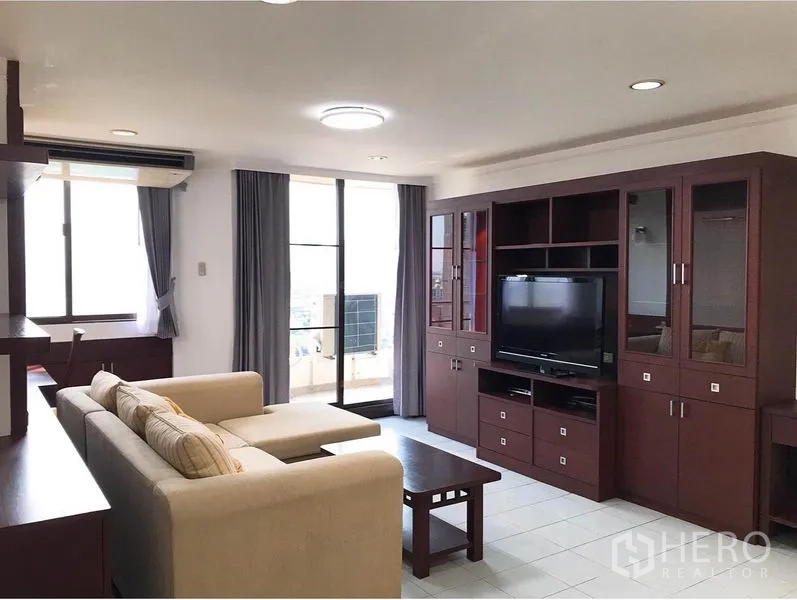 คอนโด ให้เช่าหรือขายในWatthana, Bangkok - ห้องนั่งเล่นสว่าง โซฟา L สีครีม ชุดตู้ทีวีไม้เข้ม และประตูกระจกออกระเบียง