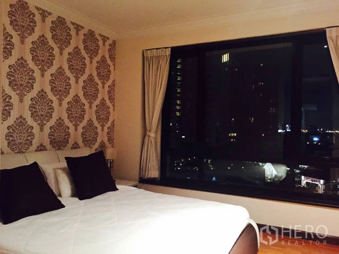 คอนโด ให้เช่าในSathon, Bangkok - ห้องนอนมีผนังลายวอลล์เปเปอร์ เตียงขนาดใหญ่ และหน้าต่างกว้างมองเห็นสกายไลน์ยามคืน