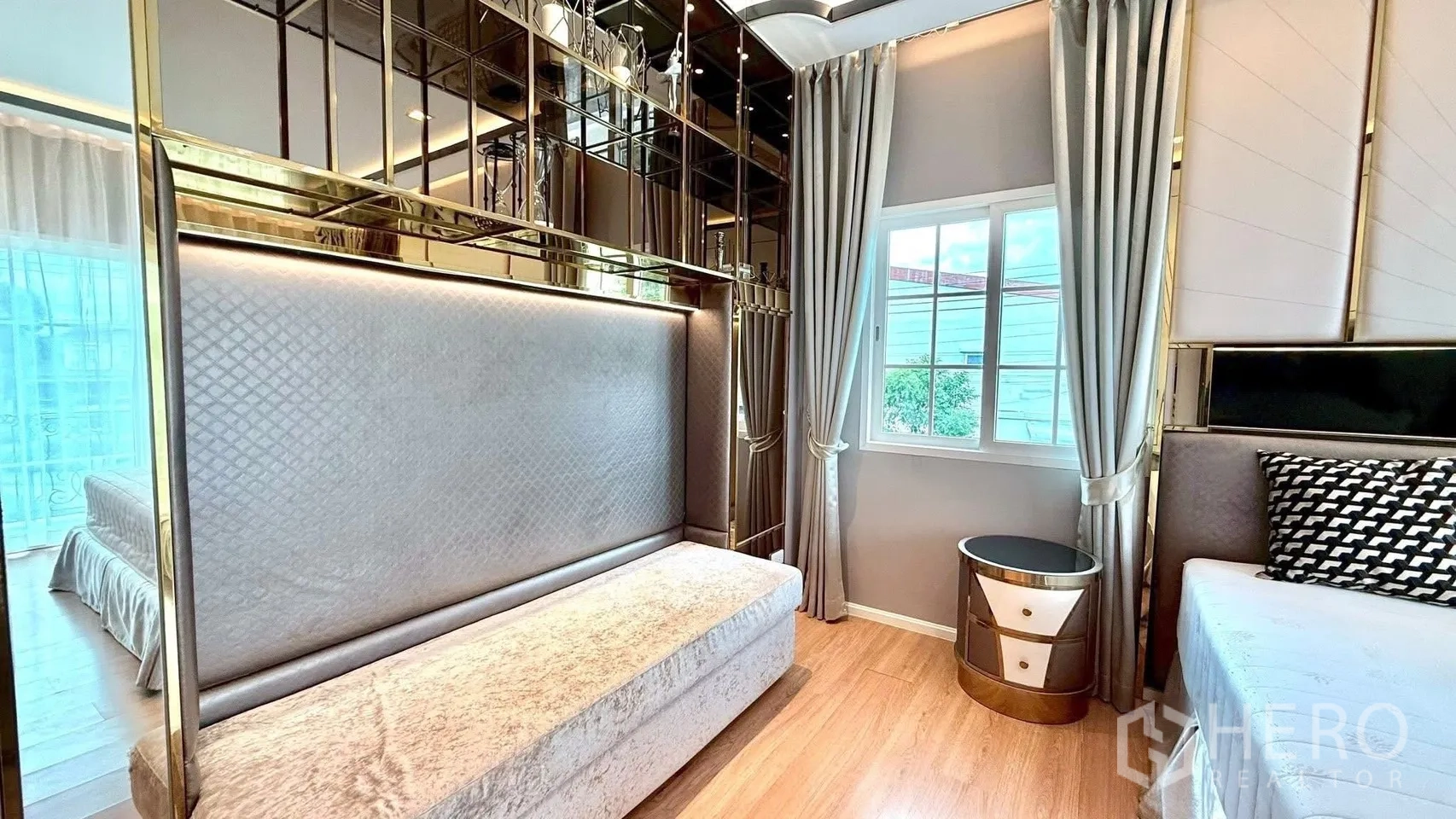 Detached House for rent or sale in Bueng Kum, Bangkok - Bedroom featuring padded headboard, mirrored wall with gold trim, side table and window.
