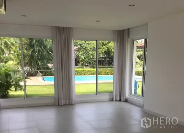 独立式住宅 出租在Bang Phli, Samut Prakan - 家庭起居室落地窗，俯瞰花园与游泳池。