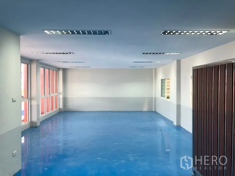 Factory for rent in Samut Prakan - Large air-conditioned office room with blue epoxy floor and wide windows for natural light.