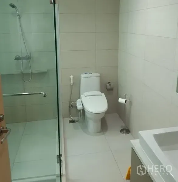 Condominium for rent in Khlong Toei, Bangkok - Modern bathroom featuring a glass shower enclosure, white tiles and contemporary fixtures.
