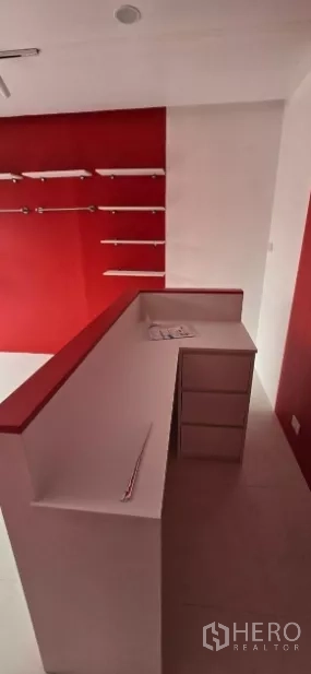 พื้นที่ขายของ for rent in Watthana, Bangkok - เคาน์เตอร์แคชเชียร์รูปตัวแอลสีขาวพร้อมลิ้นชัก ข้างผนังโชว์สินค้าสีแดงและไฟราง